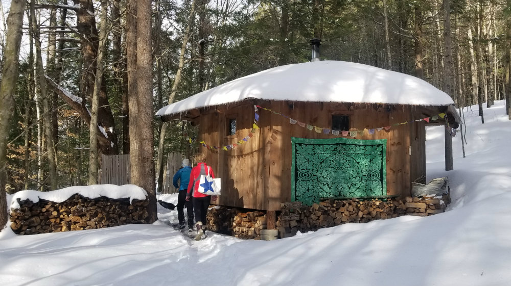 wood sauna set in the woods blanketed by fresh snow and sun shining through the trees